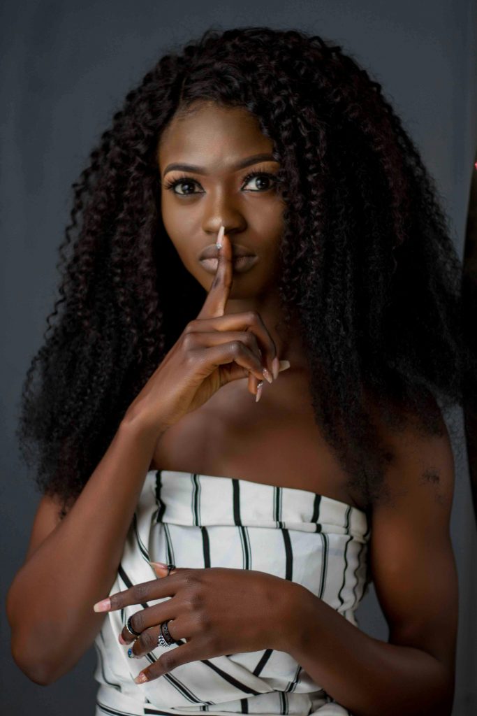 Portrait of a woman with finger on lips, indicating silence, on a dark background.