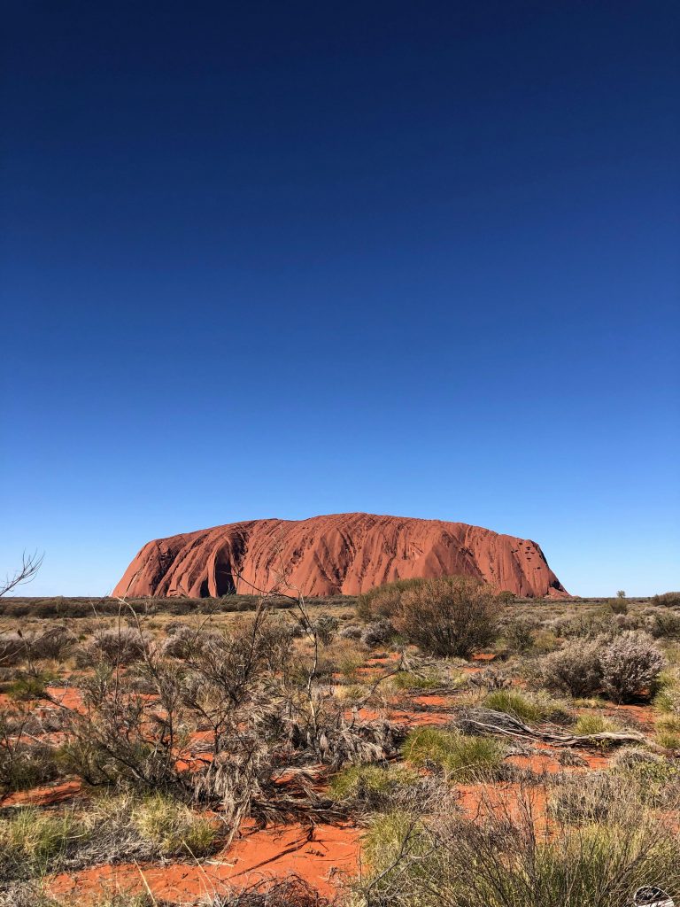 Iconic Uluru rock formation in Australia captured under a vibrant blue sky. Perfect for nature enthusiasts and travel inspiration.