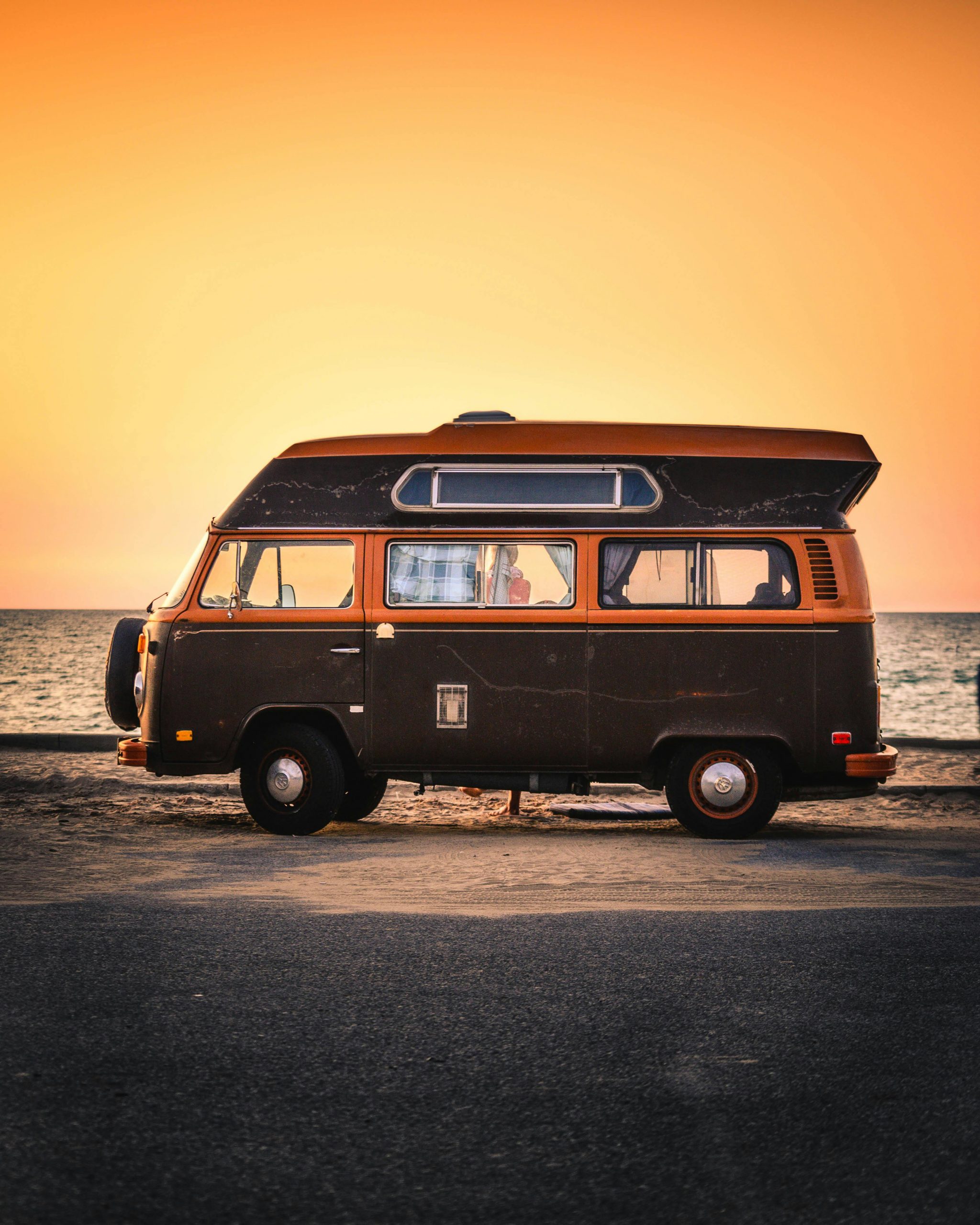 A classic Volkswagen campervan parked by the sea during a vibrant sunset.