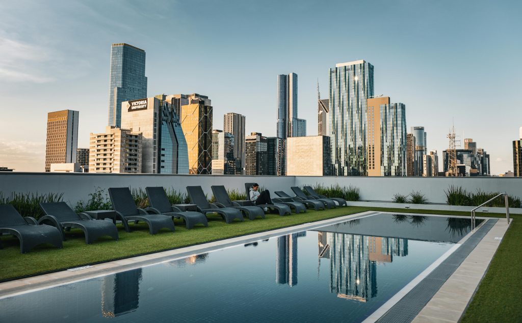Rooftop pool overlooking modern city skyline with lounge chairs, perfect for relaxation and leisure.