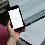 A close-up of a hand holding a smartphone displaying a loading screen over books and a laptop.