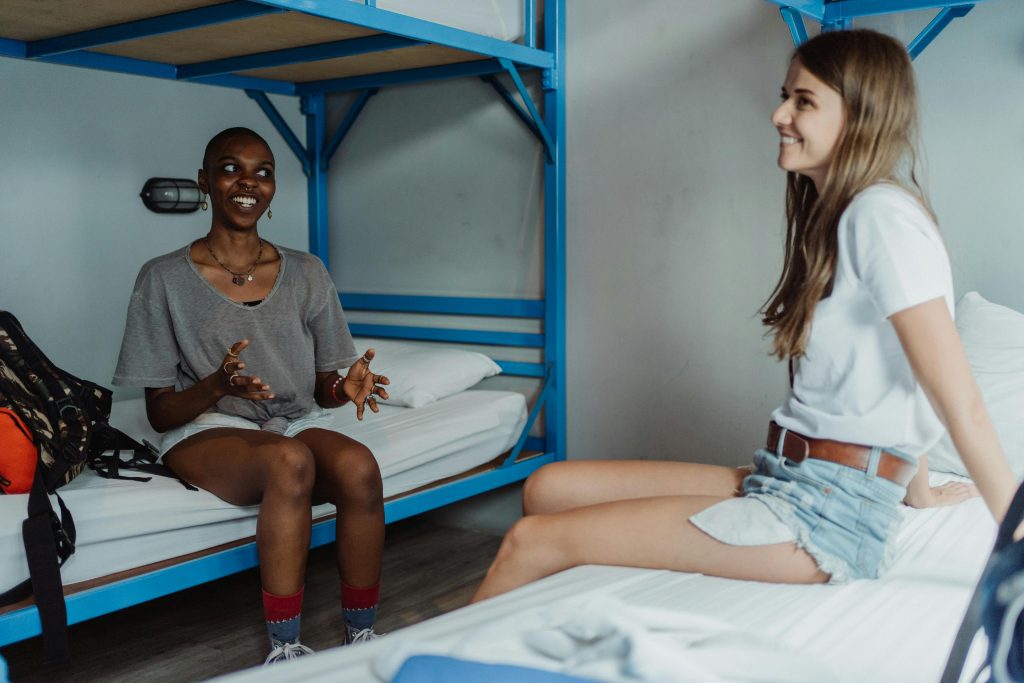 Two young women enjoying a conversation in a cozy hostel room with bunk beds.