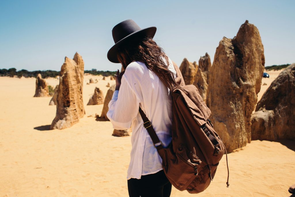 Backpacker with hat exploring rock formations in a sandy desert landscape.