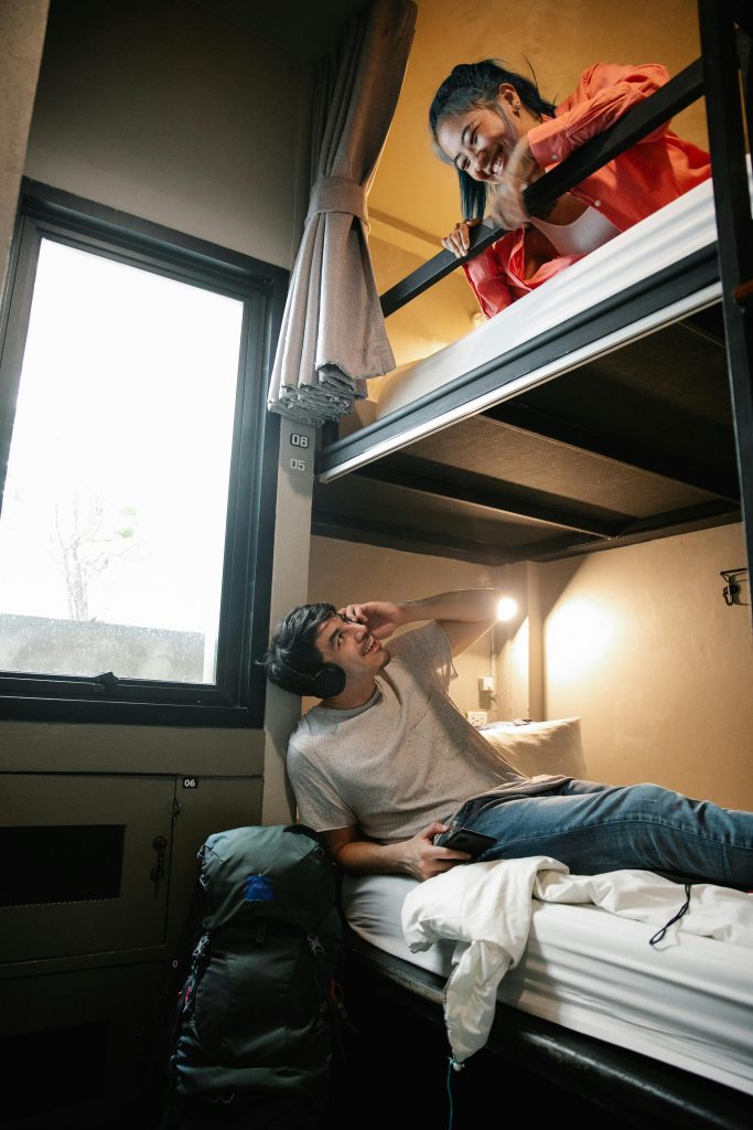 Two young adults enjoying a conversation in a cozy hostel room with bunk beds.