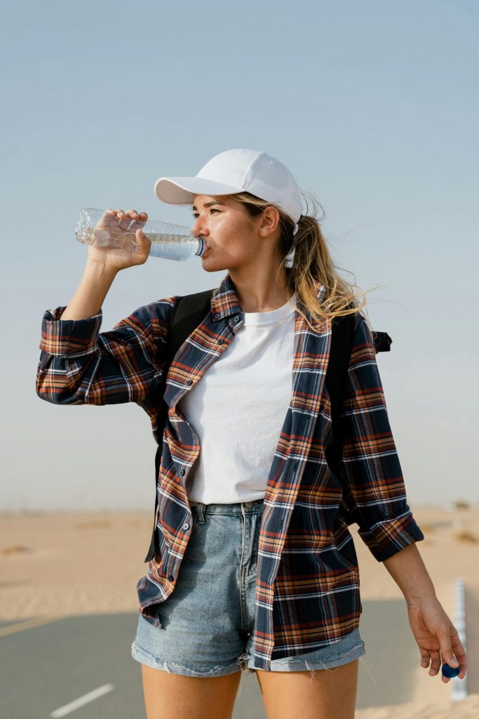 A young woman hydrates while exploring a sunny desert environment.